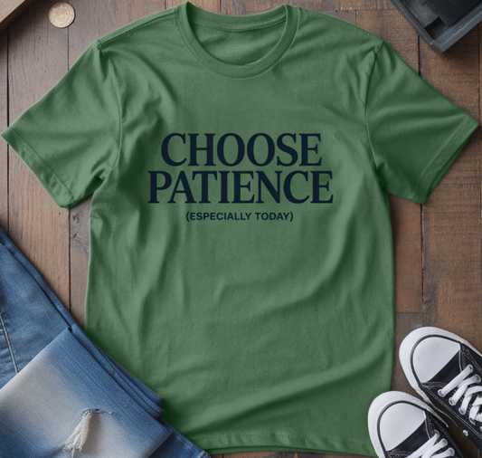 Green t-shirt with 'CHOOSE PATIENCE (ESPECIALLY TODAY)' text on a wooden surface with jeans and sneakers.