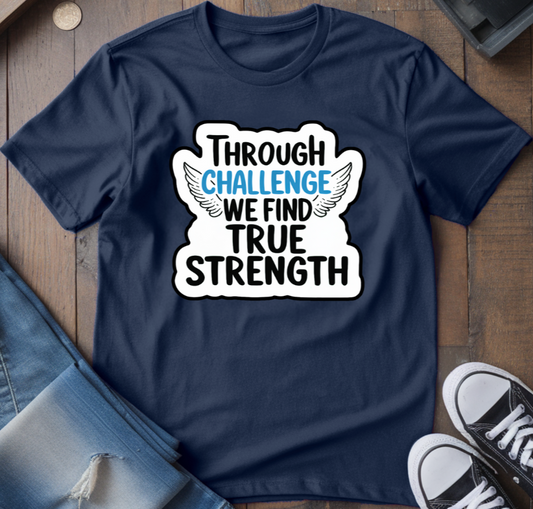 A navy blue crew neck t-shirt with the text 'THROUGH CHALLENGE WE FIND TRUE STRENGTH' printed on the front, displayed flat with jeans and sneakers on a wooden surface.